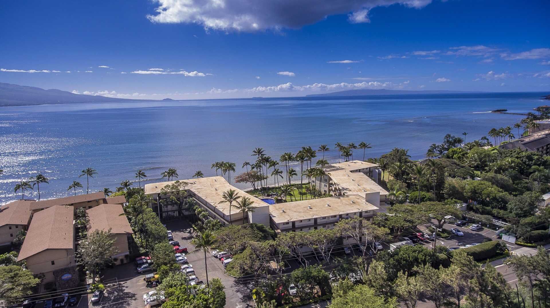 A coastal hotel with multiple buildings, a parking lot, and a view of the ocean.