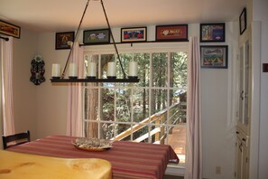 A dining area with a table set for two, a chandelier, and a window with a view of a wooden deck and trees. - Clover Cabin In The Sequoia National Forest, not near the National Park (Camp Nelson)