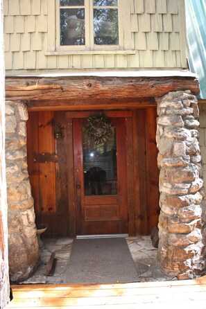 A wooden front door with a stone pillar, a window above, and a doormat. - Clover Cabin In The Sequoia National Forest, not near the National Park (Camp Nelson)