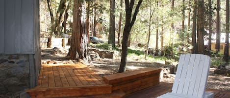 A wooden deck with a white chair, surrounded by trees and a stone wall.