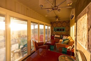 A room with a dining table, chairs, a sofa, and a large window with a view.