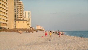 Ein Strand mit einer Holzpromenade, einigen Personen und Gebäuden im Hintergrund.