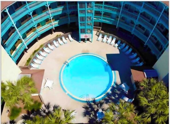 A circular pool surrounded by lounge chairs and palm trees, with a multi-level building in the background.