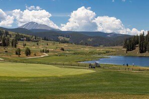 A golf course with a lake, forested hills, and a mountain in the background.