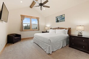 A bedroom with a bed, a nightstand, a chair, a ceiling fan, a window with curtains, and a painting on the wall.