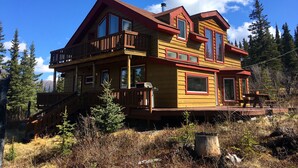 A two-story wooden cabin with a balcony, surrounded by trees and a clear sky. - ☆ Denali Sunset House - Wild scenery with creature comforts! (Denali National Park)