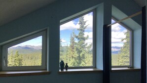 A room with three large windows offering views of a forest and mountains. - ☆ Denali Sunset House - Wild scenery with creature comforts! (Denali National Park)