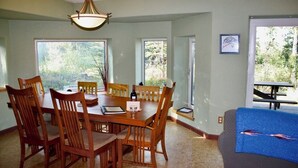A dining area with a wooden table and chairs, a chandelier, and large windows offering a view of the outdoors. - ☆ Denali Sunset House - Wild scenery with creature comforts! (Denali National Park)