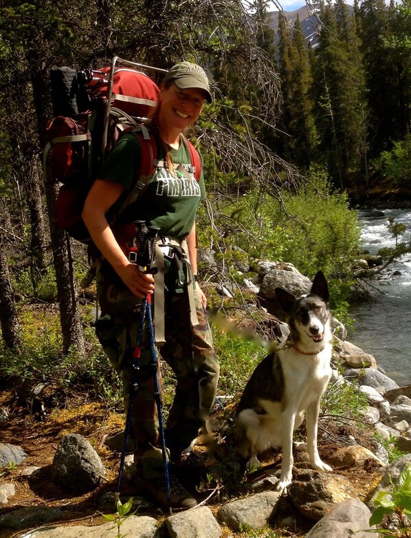 A person with a backpack and a dog sitting on rocks by a river.