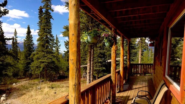 A wooden deck with chairs, surrounded by trees and a mountain view. - ☆ Denali Sunset House - Wild scenery with creature comforts! (Denali National Park)