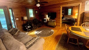 A cozy cabin interior with a wooden ceiling, a sofa, a coffee table, a TV, and a bed. - Cabin in the Big South Fork/Pickett State Park Area. (Jamestown)
