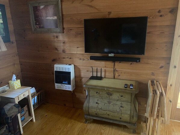 Une pièce aux murs lambrissés, avec un téléviseur fixé au mur, un petit radiateur et une commode de style ancien.