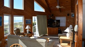 Een gezellig interieur van een blokhut met een grote televisie, houten meubels en grote ramen die uitzicht bieden op de natuur.