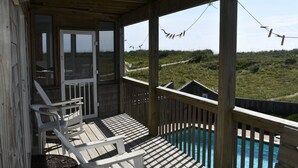 Een houten terras met zwembad, stoelen en uitzicht op het strand.
