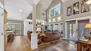 A spacious living area with a high ceiling, a fireplace, and a dining area with wooden furniture. - Bend Getaway in RiverWild-Walk to Deschutes River and Old Mill District (Bend)