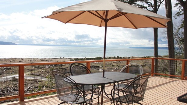 A deck with a table and chairs, an umbrella, and a view of the sea.