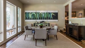 A dining area with a round table, six chairs, a large abstract painting above the table, and a dark wood cabinet to the right. - Renovated, refined, immaculate single-story mountain home 2 miles south of Baldy (Hailey)
