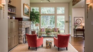 A spacious living room with a fireplace, red armchairs, a glass coffee table, and large windows offering a view of the outdoors. - Renovated, refined, immaculate single-story mountain home 2 miles south of Baldy (Hailey)