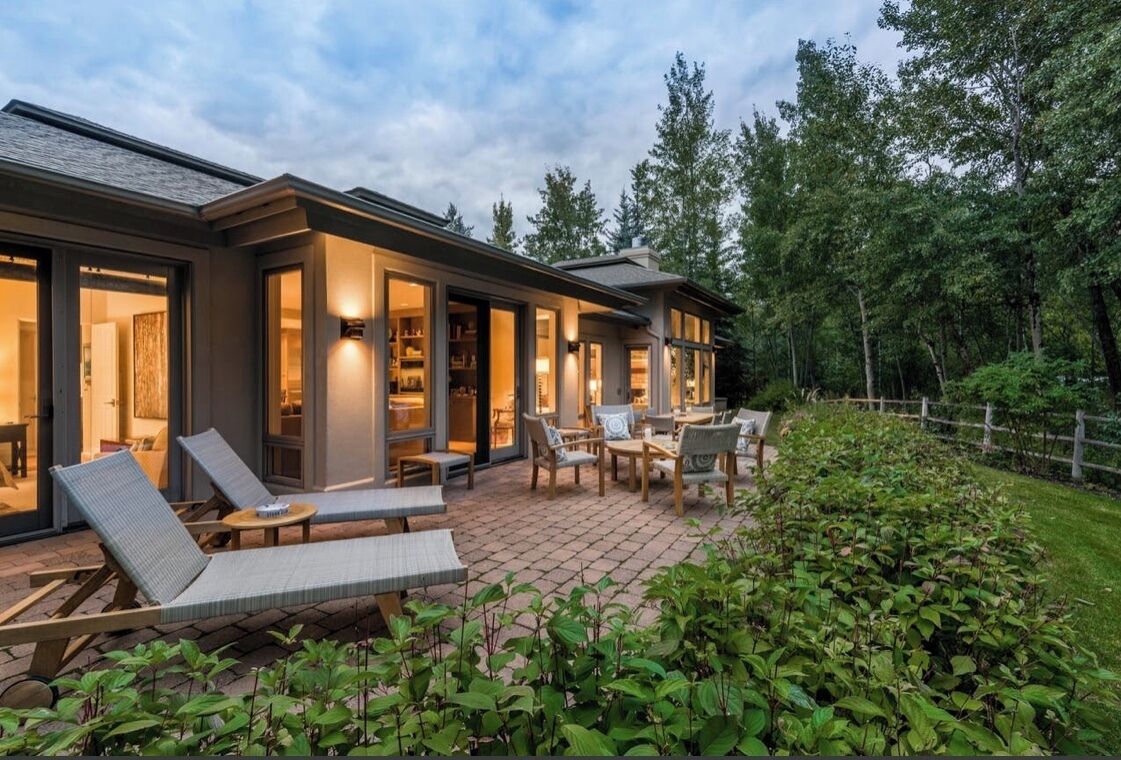 Ett modernt hus med en uteplats som har utemöbler och en välskött trädgård.
