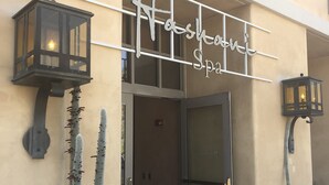 Fasaden på en byggnad med en skylt som visar texten ”Hashawi Spa”. Framför ingången står två krukväxter med kaktusar, och på var sin sida om dörren hänger två väggmonterade lyktor.
