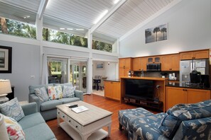 A spacious living area with a large TV, wooden cabinets, and a dining area with glass doors. - SeaPines, 31 Lighthouse, Pets OK, Walk to the Beach Club, Golf View, Updated (Hilton Head Island)
