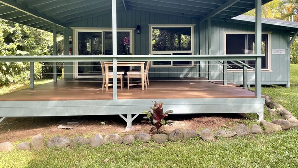 A covered outdoor area with a wooden deck, a table and chairs, and a sign reading "Tradewenda Cottage." - Secluded cottage on Tropical flower farm (Hana)
