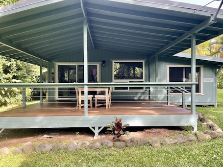 A covered outdoor area with a wooden deck, a table and chairs, and a sign reading "Tradewenda Cottage."