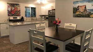 A modern kitchen with white cabinets, a central island, and a dining table with chairs. - Secluded cottage on Tropical flower farm (Hana)