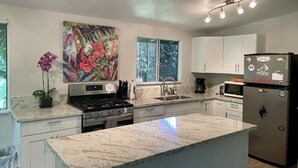 A modern kitchen with white cabinets, a granite countertop, a stainless steel stove, and a refrigerator with magnets. - Secluded cottage on Tropical flower farm (Hana)