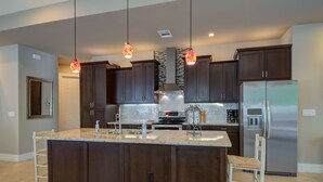 Een moderne keuken met donkerhouten kastjes, een groot eiland met een marmeren aanrechtblad, roestvrijstalen apparatuur en hanglampen.