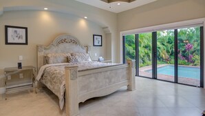Een ruime slaapkamer met een groot bed, een nachtkastje en uitzicht op een zwembad door grote schuifdeuren.