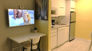 A modern kitchen with white cabinets, a microwave, a refrigerator, and a flat-screen TV mounted on the wall.