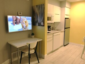 Una cocina moderna con armarios blancos, un microondas, un refrigerador y un televisor de pantalla plana montado en la pared.