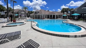 A swimming pool area with multiple pools, lounge chairs, and umbrellas.