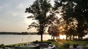 A serene lakeside garden with a gazebo, a fountain, and a well-maintained flower bed.