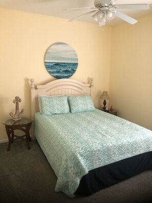 Een slaapkamer met een bed, een ronde wanddecoratie, een plafondventilator, een klein tafeltje met een lamp en een decoratief anker.
