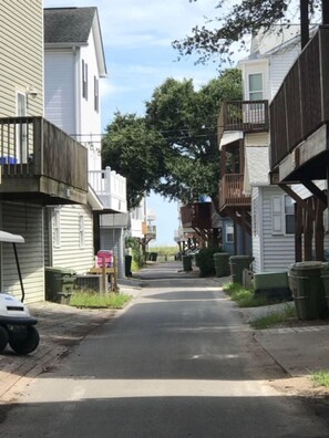 Een smalle straat met twee verdiepingen hoge huizen, waarvan sommige balkons hebben, onder een heldere lucht.