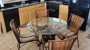 A kitchen with a round glass table surrounded by wicker chairs, wooden cabinets, a black refrigerator, and a window with a view of greenery. - Middle Bass Island-Premium Lakefront Condo with Large Lakefront Covered Patio  (Middle Bass Island)