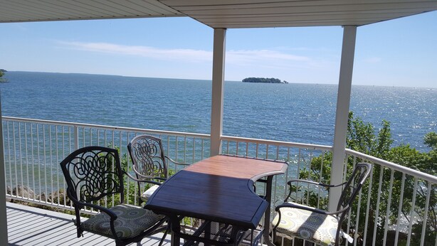 A covered outdoor seating area with a table and chairs, overlooking a body of water and a distant island. - Middle Bass Island-Premium Lakefront Condo with Large Lakefront Covered Patio  (Middle Bass Island)