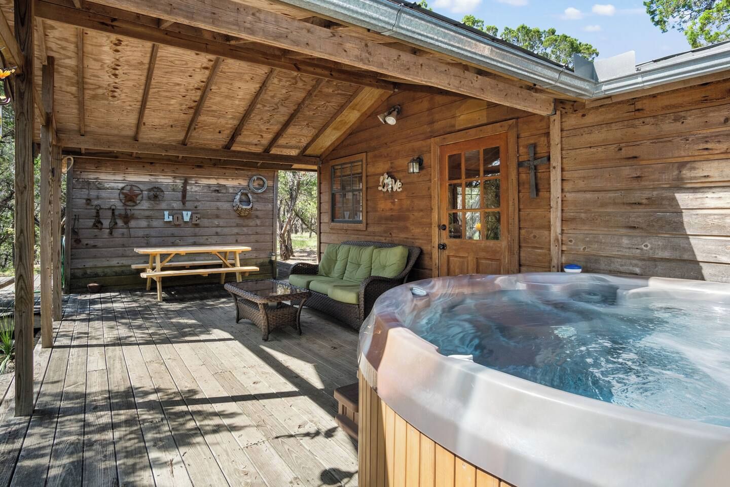 A wooden cabin with a hot tub, a picnic table, and a sofa.