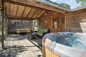 A wooden cabin with a hot tub, a picnic table, and a sofa.