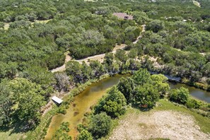 An aerial view of a property with a river, dense greenery, and a small building. - Love Shack | Romantic Cabin w/ Hot Tub & Creek (Pipe Creek)