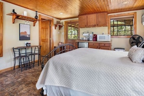 A bedroom with a bed, a desk, and a chair. There is a window with a view of trees. - Love Shack | Romantic Cabin w/ Hot Tub & Creek (Pipe Creek)