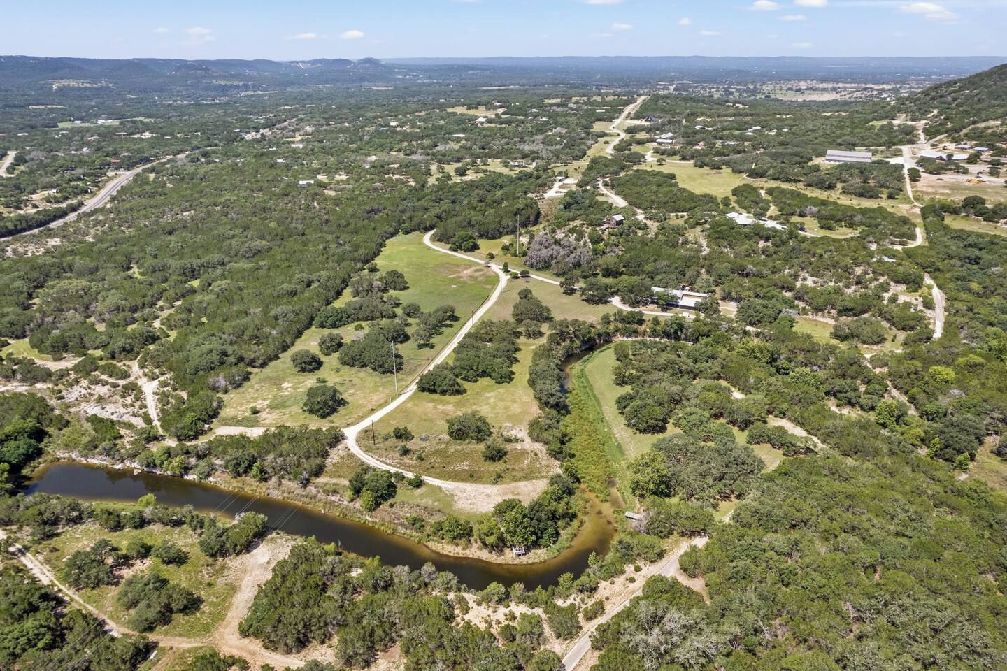 Vista aerea di un parco con sentieri sinuosi, un fiume e edifici sparsi.