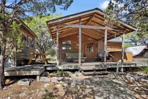 A rustic cabin with a covered porch, a wooden deck, and a hot tub. - Love Shack | Romantic Cabin w/ Hot Tub & Creek (Pipe Creek)