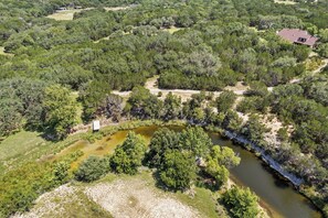 An aerial view of a property with a river, dense greenery, and a small building. - Love Shack | Romantic Cabin w/ Hot Tub & Creek (Pipe Creek)