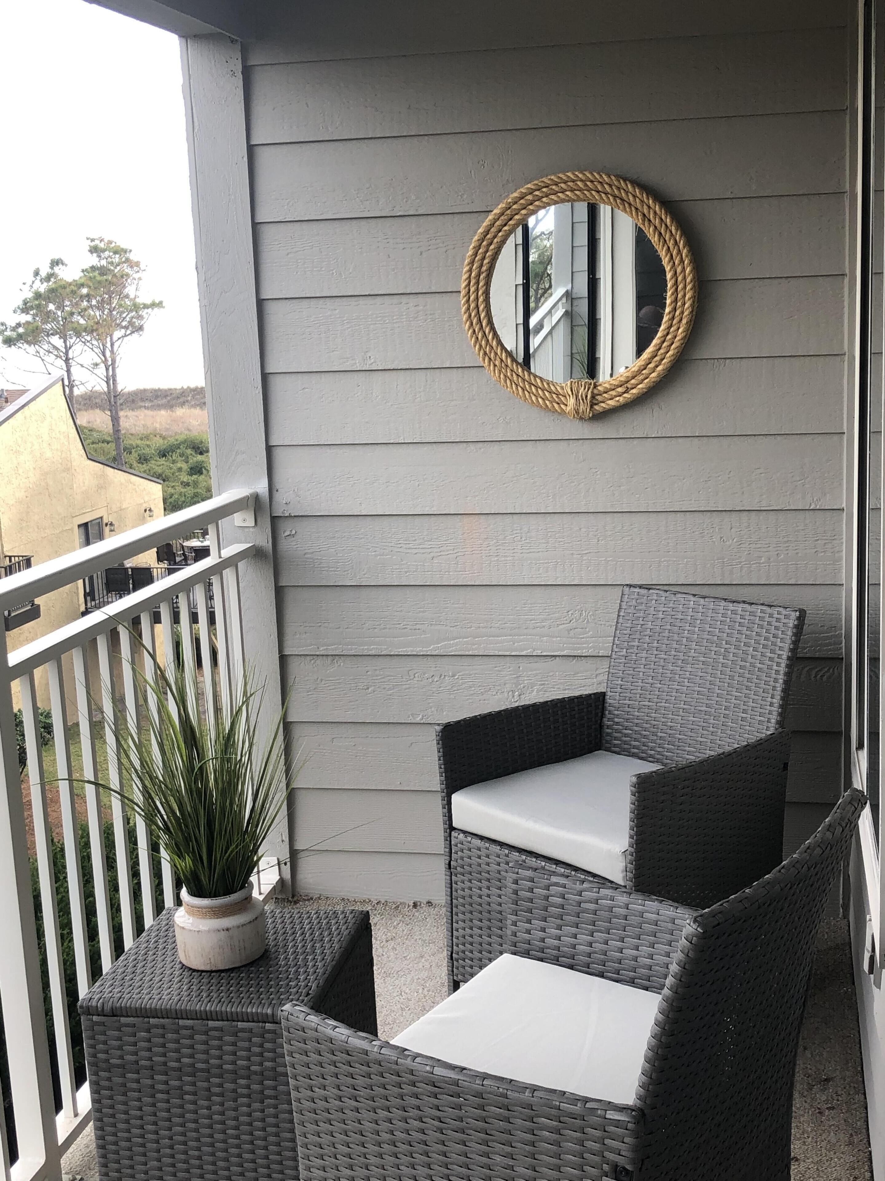 A balcony with wicker furniture, a potted plant, and a round mirror on the wall.