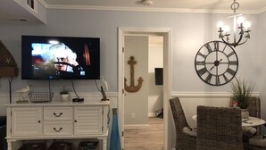 Ein Wohnzimmer mit Fernseher, weißem Schrank, Korbstühlen und einer großen Wanduhr.