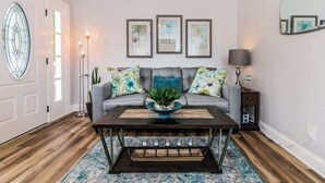 Un salon avec un canapé, une table basse, un lampadaire et des œuvres d’art encadrées accrochées au mur.