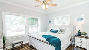 Une chambre à coucher avec un lit, un ventilateur de plafond, une table de chevet et une fenêtre avec des stores.